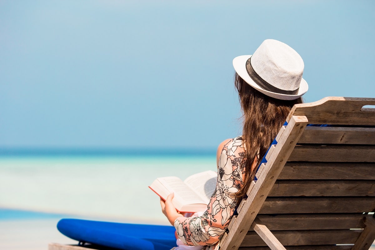 Portrait Of A Young Woman Relaxing On The Beach, Reading A Book