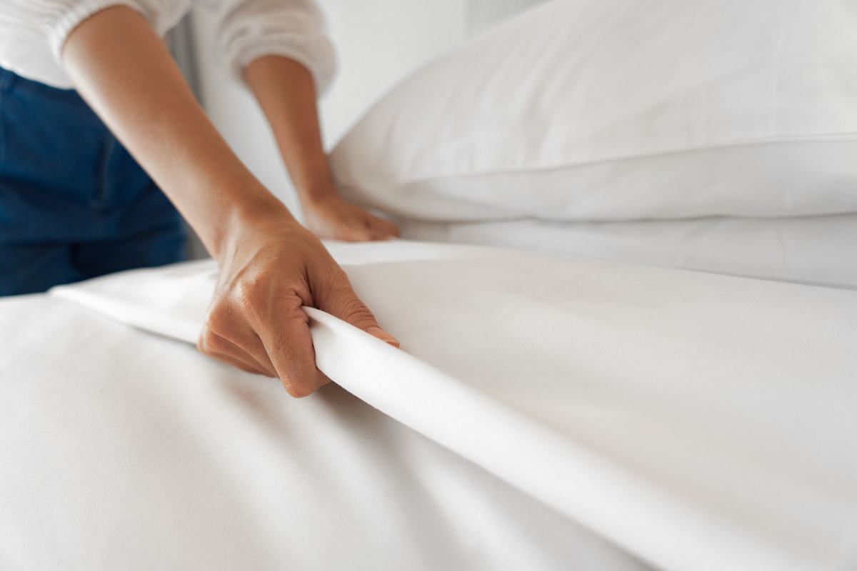 Female Hand Set Up White Bed Sheet In Bedroom